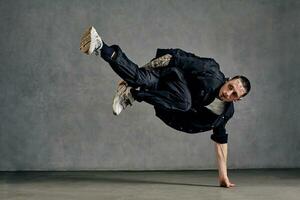 actief Mens met getatoeëerd lichaam, baard. gekleed in wit t-shirt en sportschoenen, zwart shirt, broek. dansen Aan grijs achtergrond. danszaal, hiphop foto