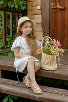 preteen meisje zittend Aan drempel van land huis met bundel van wilde bloemen in mand foto