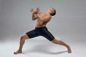 foto van een knap Mens ballet danser, gekleed in een zwart korte broek, maken een dans element tegen een grijs achtergrond in studio.