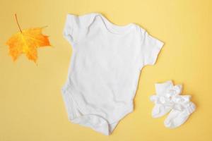 baby clobodysuit-model met esdoornblad op gele achtergrond voor uw tekst of logo in het herfstseizoen foto