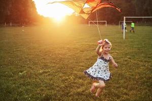 schattig klein meisje met lang haar met vlieger in het veld op zonnige zomerdag