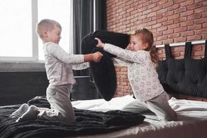 stoute kinderen kleine jongen en meisje voerden een kussengevecht op het bed in de slaapkamer. ze houden van dat soort spel