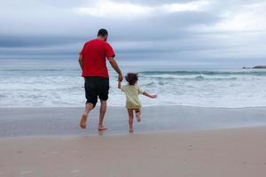 vader en zoon lopen op zomer strand. vader en kind plezier buitenshuis. foto