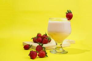 een glas van melk met aardbei garneer Aan besnoeiing bord geïsoleerd geel achtergrond foto