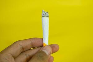 een Mens hand- houdt een handgemaakt sigaret Aan geel achtergrond foto