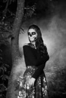 portret van jong vrouw met bang halloween bedenken in bos. halloween maken omhoog suiker schedel mooi model- met perfect kapsel. duivel meisje concept. foto