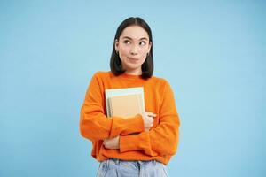 glimlachen Aziatisch vrouw met notitieboekjes, leerling met gelukkig gezicht, promo van college opleiding, blauw achtergrond foto