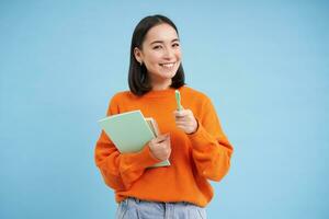 onderwijs en studenten. gelukkig Aziatisch vrouw, Holding notebooks en lachend, glimlachen Bij camera, geniet gaan naar Universiteit of middelbare school, blauw achtergrond foto