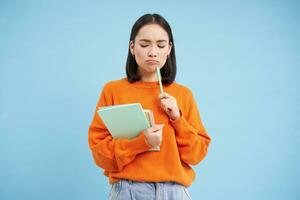 onderwijs en studenten. gelukkig Aziatisch vrouw, Holding notebooks en lachend, glimlachen Bij camera, geniet gaan naar Universiteit of middelbare school, blauw achtergrond foto