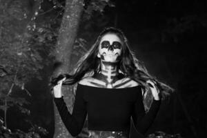 portret van jong vrouw met bang halloween bedenken in bos. halloween maken omhoog suiker schedel mooi model- met perfect kapsel. duivel meisje concept. foto