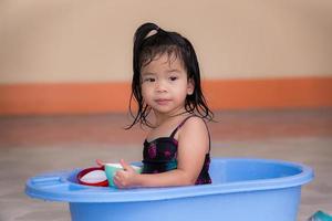 meisje in badpak, spelend in het blauwe bassin voor haar huis. kinderen spelen plastic bekers, speelgoed uit de omgeving in het dagelijks leven. schattig klein kind, 3 jaar oud.
