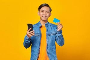 portret van glimlachende aziatische man die creditcard gebruikt om met mobiele telefoon te betalen foto