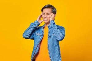 jonge aziatische man die hoofdpijn voelt op gele achtergrond foto