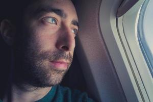 close-up van een peinzende man die door het raam van een vliegtuig naar buiten kijkt foto