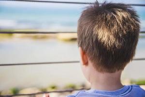 jonge jongen kijkt ver weg naar de horizon van achter een metalen hek