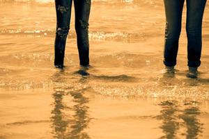 vrouwenbenen in spijkerbroek die in het zeewater aan de kust staan - gouden toon