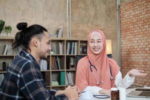 jonge mooie vrouw arts is gezondheid die mannelijke patiënt onderzoekt in het kantoor van de ziekenhuiskliniek en met een glimlach adviseert over medicijnen. deze aziatische medisch specialist is een islamitisch persoon die een hijab draagt. foto