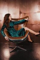 mooi meisje in fluwelen jurk, zittend in leren bruine fauteuil