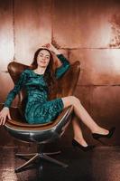mooi brunette meisje in een fluwelen jurk, zittend in een leren fauteuil foto