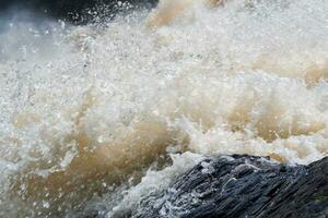 modderig turbulent stroom onder een rots gedurende hoog water foto