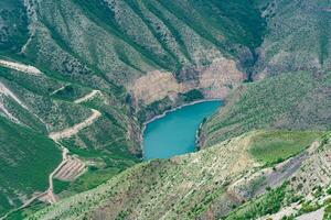 berg landschap, diep Ravijn met een blauw rivier- Bij de bodem foto