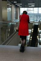 jong vrouw in een rood jas staat met haar terug naar de kijker in de lobby van een openbaar gebouw foto