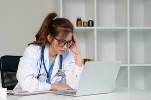 benadrukt jong vrouw dokter op zoek Bij laptop, werk verwant chaos, bezorgd over vergissing Bij werk de gestrest, ongelukkig medisch professioneel is moe van oplossen computer problemen Bij werk. foto