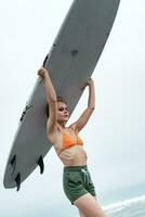 vrouw surfer draag- surfboard Aan hoofd gedurende sport- opleiding. vrouw in bikini top en shorts foto