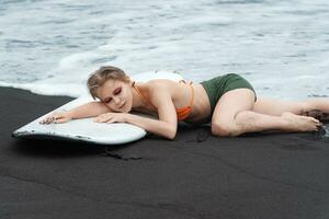 surfer leugens Aan surfboard Aan strand, ogen gesloten, gevoel warmte van zon en teder zwaaien van oceaan foto