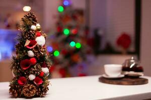 dichtbij omhoog van Kerstmis boom in feestelijk keuken georganiseerd voor winter avondeten feest. niemand in leeg helder kamer met verlichte slinger ornamenten, Koken gereedschap en houten interieur foto