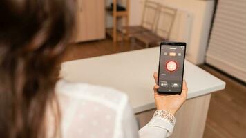 vrouw in huis keuken gebruik makend van telefoon app naar van een afstand controle verlichting systeem. persoon in appartement Holding telefoon met touch screen en app voor lichten. foto