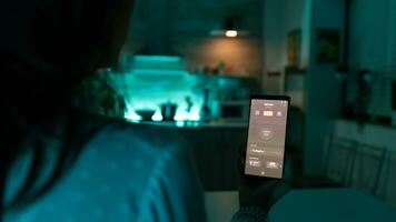 vrouw in huis donker kamer gebruik makend van automatisering app voor verlichting. persoon in appartement Holding telefoon met touch screen en app voor lichten. foto