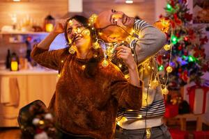 grappig paar vangen in Kerstmis boom licht gedurende kersttijd voorbereidingen treffen decoratie voor keuken. gelukkig familie genieten van uitgeven winter vakantie samen. Kerstman feestelijk traditie foto