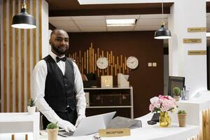 Afrikaanse Amerikaans loopjongen werken Bij hotel, zorgen voor professioneel luxe conciërge Diensten voor gasten. mannetje toevlucht werknemer het verstrekken van bijstand Bij controleren in, helpen met accommodatie. foto