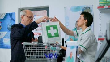 apotheek werknemer Bij apotheek teller scannen farmaceutisch producten van ouderen cliënt boodschappen doen mand. oud Mens buying kwaal verbeterend geneesmiddelen in apotheek foto