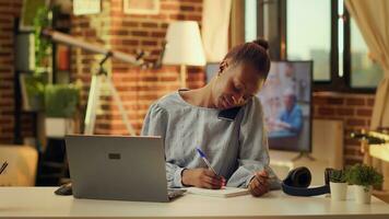 freelancer schrijven aantekeningen van telefoon telefoontje Bij huis kantoor, gebruik makend van handschrift naar hebben lijst van informatie over toekomst taken. vrouw gebruik makend van notitieboekje naar creëren perfect project. foto