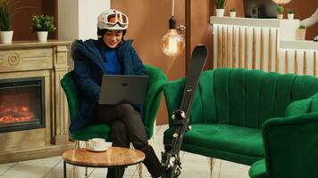 persoon lezing plaats beoordelingen Aan laptop Bij luxe ski toevlucht, zittend in lobby met skiën uitrusting en accessoires. Aziatisch vrouw werken afgelegen Aan draadloze pc voordat beoefenen extreem winter sport. foto