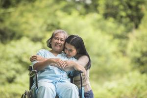 kleindochter praten met haar grootmoeder zittend op rolstoel, vrolijk concept, gelukkig gezin foto