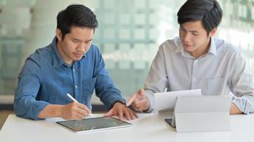 twee aziatische mannen gebruiken tablet om hun werk te maken om klanten in een eigentijds kantoor te presenteren. foto