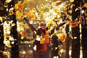 vrolijke jonge vrouw gooit esdoornbladeren op een zonnige dag in de herfst foto