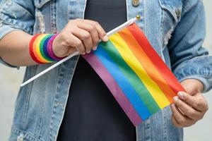 aziatische dame die een blauw spijkerjack of een denimoverhemd draagt en een regenboogvlag vasthoudt, symbool van de lgbt-trotsmaand viert jaarlijks in juni sociaal van homo, lesbienne, biseksueel, transgender, mensenrechten. foto