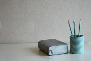 een boek en pastelpotloden in het blauwe glas op het bureau bij een grijze muurachtergrond foto