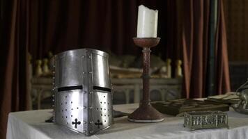 middeleeuws interieur met details en voorwerpen. actie. zilver ridder helm en kaars staan Aan tafel in middeleeuws interieur. voorwerpen van midden- leeftijden zijn Aan tafel Aan achtergrond van rood kleding stof in museum foto