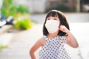 een schattig meisje met een wit hygiënisch gezichtsmasker staat op te kijken. kinderen denken en vragen zich af wat ze 's ochtends zien. foto