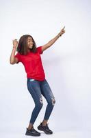 mooie jonge afrikaanse dame met een rode top en een blauwe spijkerbroek die opgewonden is en naar haar zij wijst foto