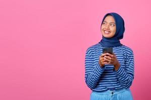 portret van glimlachende jonge aziatische vrouw die mobiele telefoon vasthoudt en opzij kijkt
