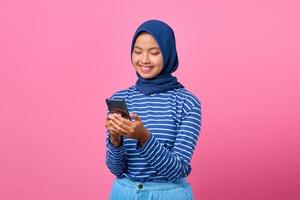portret van gelukkige jonge aziatische vrouw die mobiele telefoon op roze achtergrond gebruikt