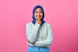 portret van glimlachende jonge aziatische vrouw die kin met hand op roze achtergrond aanraakt foto