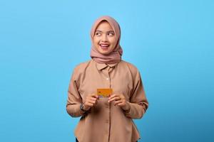 portret van een glimlachende jonge aziatische vrouw die een creditcard vasthoudt terwijl ze opzij kijkt foto