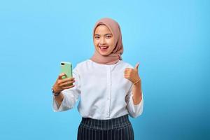 portret van een vrolijke jonge aziatische vrouw die een mobiele telefoon vasthoudt en duimen laat zien